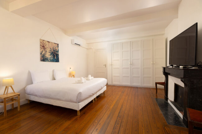 Chambre spacieuse avec lit double, grande télévision murale, sol en bois vernis et rangements intégrés