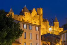 Vue rapprochée sur les remparts de la Cité de Carcassonne la nuit, surplombant une maison ancienne aux volets ouverts