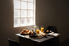 Table dressée pour le petit-déjeuner avec croissants, baguette, jus d’orange et fruits, sous une lumière naturelle