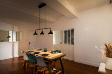 Salle à manger avec grande table en bois, décoration florale, parquet en bois foncé et lumière tamisée.