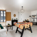 Salon de loisirs avec baby-foot, canapé clair, décoration murale et mobilier moderne, dans un appartement lumineux