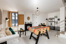 Salon de loisirs avec baby-foot, canapé clair, décoration murale et mobilier moderne, dans un appartement lumineux