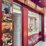 Façade rouge de trois quart de la boucherie rabat avec en premier plan une pancarte verticale faisant la promotion du cassoulet
