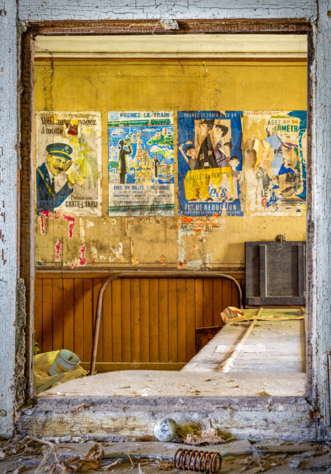 Murs jaunis d’une gare abandonnée décorés d’anciennes affiches ferroviaires.