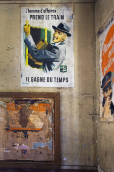 Affiche rétro SNCF dans une gare délabrée avec panneau mural abîmé.