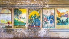 Enfilade d’anciennes affiches ferroviaires colorées sur un mur abîmé.