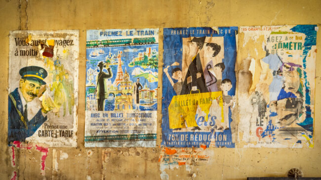 Série d’affiches ferroviaires colorées et abîmées sur un mur ancien.