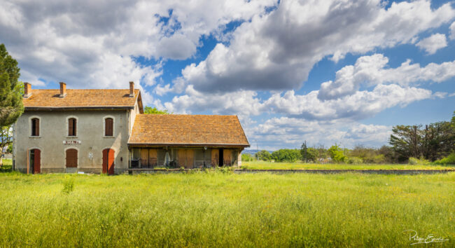 Vue large d’une gare fantôme en ruine avec prairie au premier plan