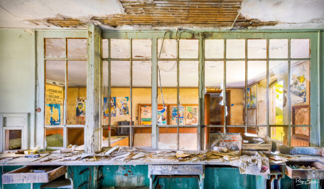 Guichet délabré d’une gare abandonnée avec vitres cassées et papiers éparpillés