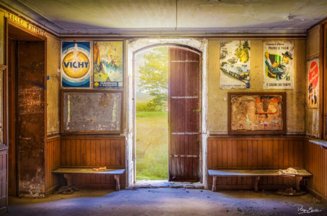 Salle d’attente de gare fantôme avec affiches anciennes et porte ouverte sur la campagne