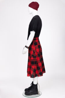 Vue de profil d’un mannequin en studio portant une jupe homme rouge et noire à carreaux, collection La Jupe qui fait mâle