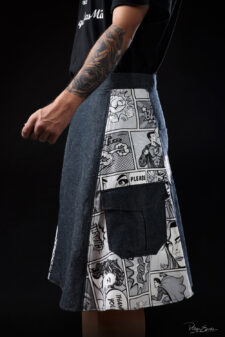 Jupe homme en jean avec empiècement imprimé bande dessinée noir et blanc, vue de profil en studio sur fond sombre