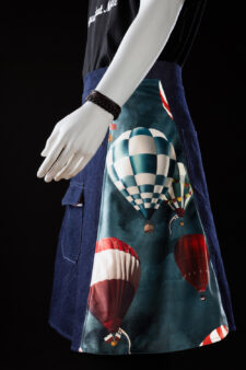 Jupe homme en jean avec empiècement imprimé montgolfières colorées, photographiée en studio sur fond noir catalogue mode