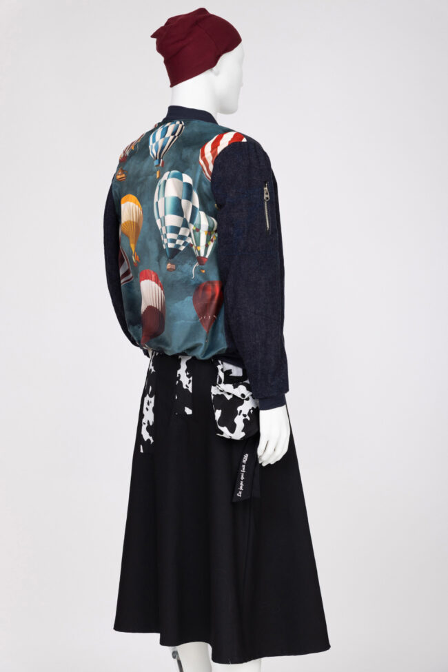 Vanessa, la fille qui glisse ses mains sous les Jupes des Hommes 10 Mannequin sur fond blanc portant une jupe noire avec motifs blanc et un blouson avec une montgolfière dessus.