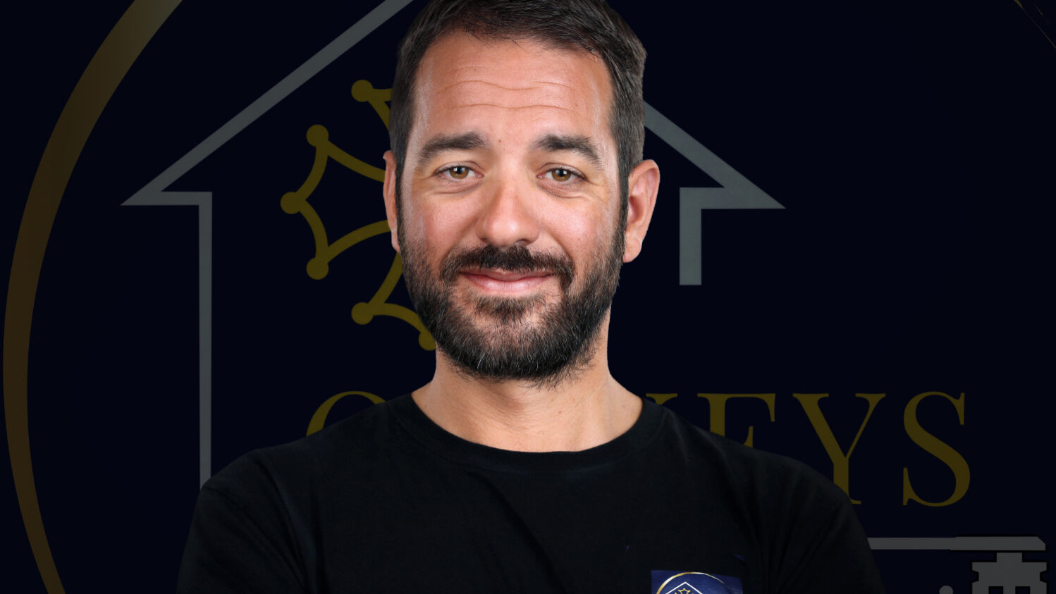 visage d'un homme barbu souriant avec un logo derrière lui en arrière plan sombre