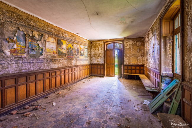 Salle d’attente délabrée avec bancs en bois et lumière entrant par la porte