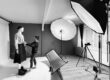 Photo noir et blanc de La créatrice Vanessa Batard qui ajuste une jupe homme sur un mannequin dans un studio photo avec des projecteurs.