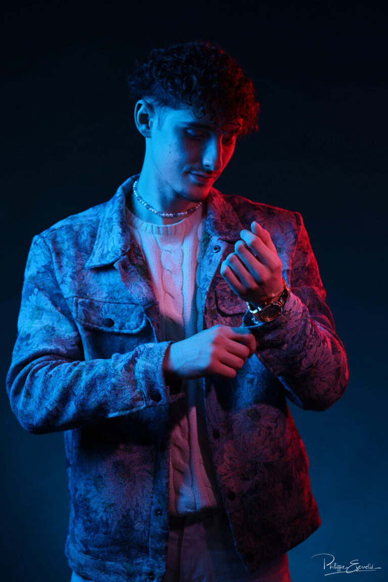 Portrait d’un modèle vérifiant sa manche sous un éclairage mixte rouge et bleu, réalisé en studio