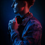 Portrait de profil d’un homme en veste texturée et casque autour du cou, éclairé par un subtil mélange de lumières rouges et bleues.