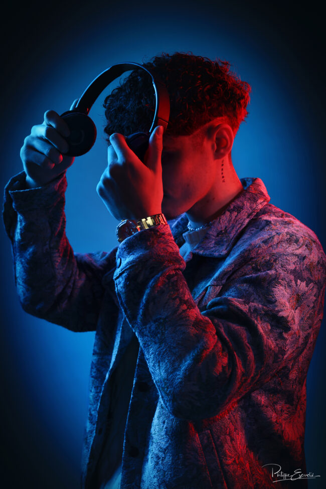 Jeune homme ajustant un casque audio sous une lumière studio rouge et bleue
