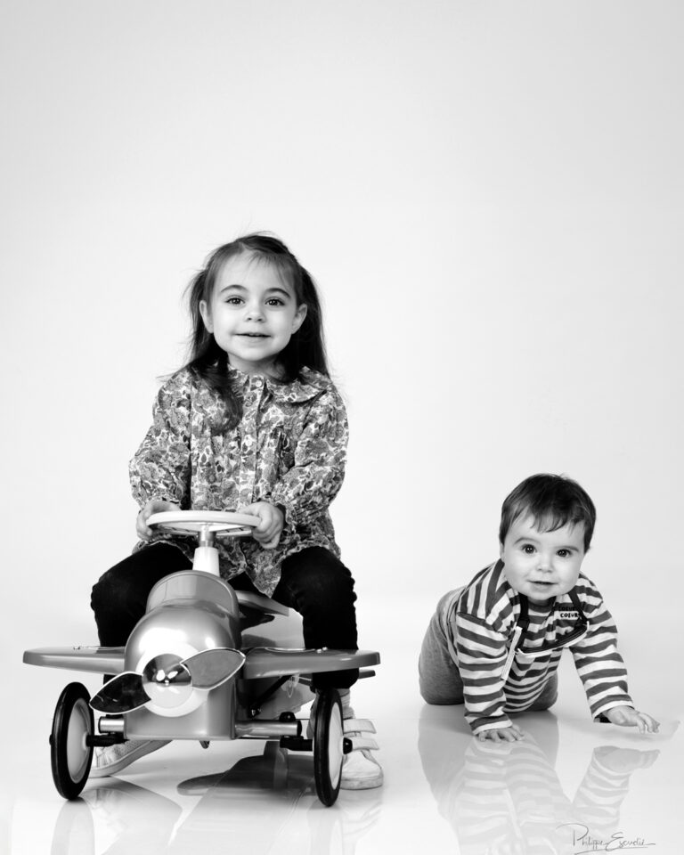 Petite fille assise sur un avion jouet avec un bébé rampant à côté en studio
