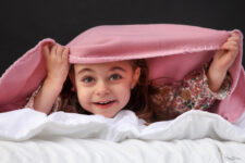 Petite fille jouant à cache-cache sous une couverture rose en studio