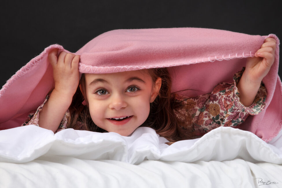 Petite fille jouant à cache-cache sous une couverture rose en studio