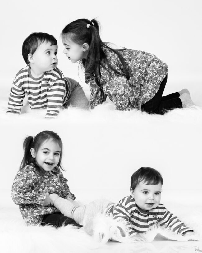 Deux enfants jouant ensemble allongés sur un tapis blanc en studio noir et blanc. On voit deux fois les enfants sur la même image.