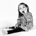 Petite fille en noir et blanc assise en studio faisant une expression surprise symbolisant la musique hard rock.