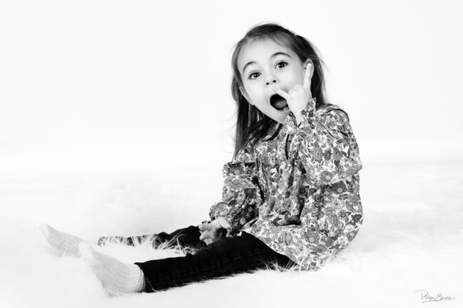 Petite fille en noir et blanc assise en studio faisant une expression surprise symbolisant la musique hard rock.