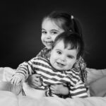 Frère et sœur enlacés et souriants sur fond noir en studio photo noir et blanc