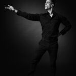 Portrait artistique en noir et blanc d’un homme adoptant une posture expressive de danse de salon sur fond sombre.