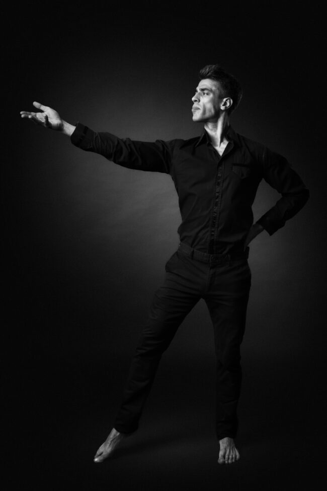 Portrait artistique en noir et blanc d’un homme adoptant une posture expressive de danse de salon sur fond sombre.