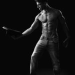 Portrait en noir et blanc mettant en valeur la silhouette athlétique d’un homme tenant un chapeau.