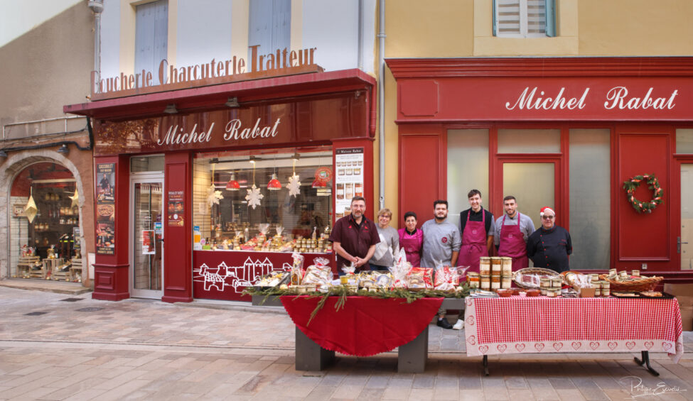 Groupe de personnes posant derrière un stand de produits alimentaires, devant une façade de commerce.