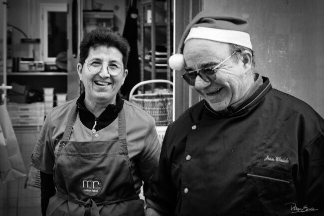 Portrait en noir et blanc de deux personnes en tenue professionnelle, souriantes, devant un espace de travail.