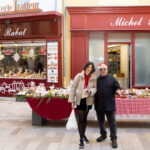 Vue d’ensemble d’un stand alimentaire en extérieur, devant des façades de commerces, avec produits disposés sur les tables.