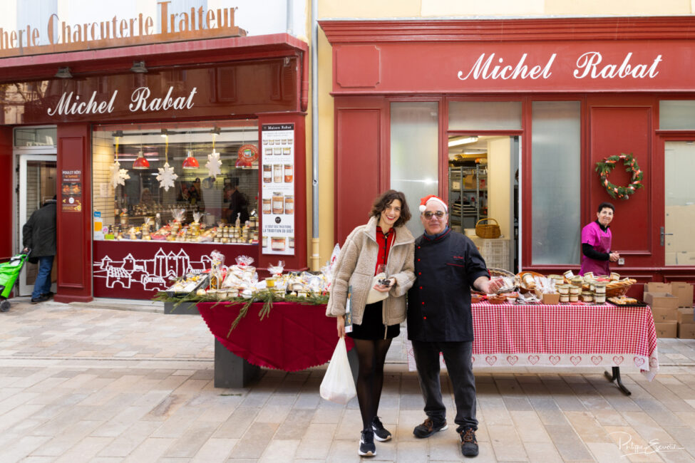 Vue d’ensemble d’un stand alimentaire en extérieur, devant des façades de commerces, avec produits disposés sur les tables.