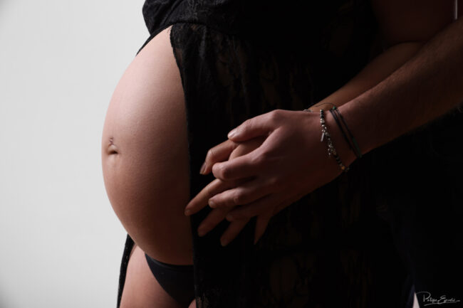 Gros plan sur les mains du futur père posées avec douceur sur le ventre arrondi de la future maman.