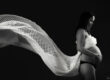 Portrait de grossesse en clair-obscur noir et blanc où un voile léger se déploie derrière la future maman, créant une image à la fois douce et graphique.