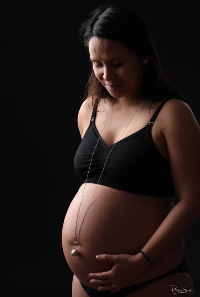 Portrait en low key d’une future maman avec un bola reposant sur le ventre, symbole de la maternité.