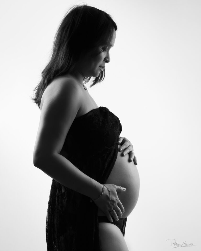 Shooting grossesse au studio photo de Carcassonne – Mai Lynh et Thomas 2 Photographie de maternité en noir et blanc montrant le profil d’une future maman avec ses mains sur son ventre arrondi dans une ambiance élégante et intemporelle.