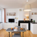 Salle à manger avec cheminée décorative, table avec petit déjeuner dressé, cuisine ouverte et décoration épurée dans un appartement rénové.