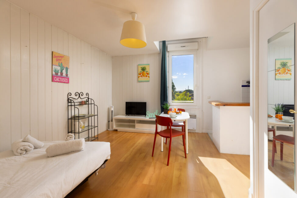 Studio meublé avec coin repas, parquet clair et grande fenêtre offrant une vue dégagée