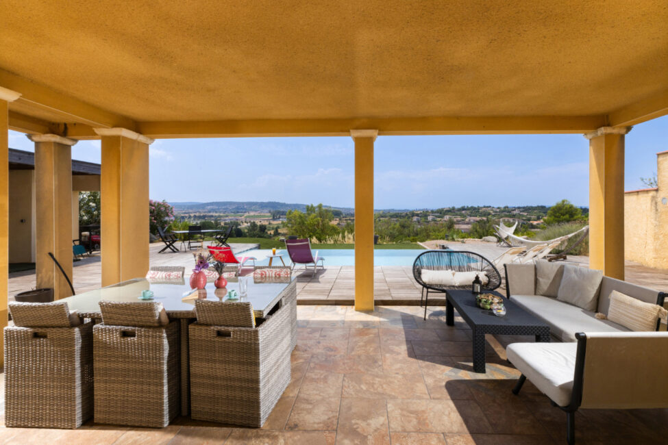 Photographe immobilier à Carcassonne : quand un shooting professionnel change tout 7 Terrasse couverte avec espace repas, salon et vue sur la piscine.