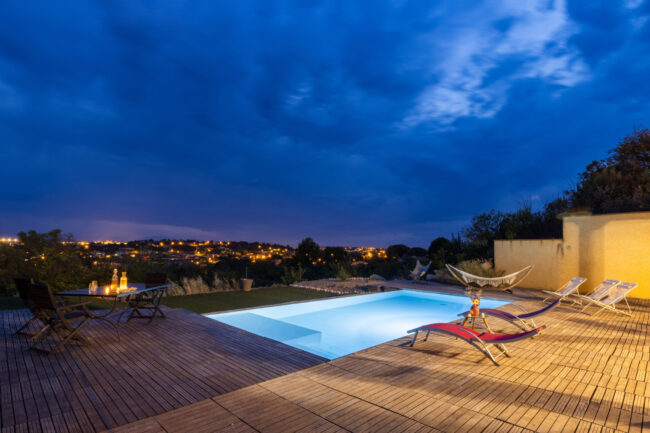 Piscine éclairée au crépuscule avec terrasse et mobilier extérieur.