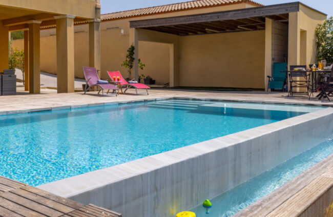Piscine extérieure bordée d'une terrasse en bois et d'un espace détente couvert.