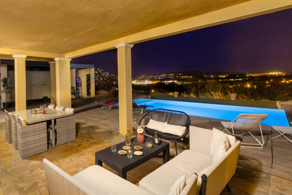 Photographe immobilier à Carcassonne : quand un shooting professionnel change tout 14 Terrasse couverte avec salon extérieur et piscine illuminée de nuit.
