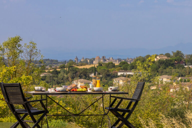 Photographe immobilier à Carcassonne : quand un shooting professionnel change tout 1 Terrasse aménagée avec petit-déjeuner offrant une vue panoramique sur la Cité de Carcassonne.