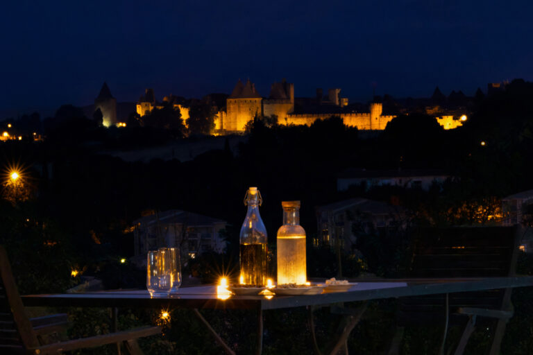 Photographe immobilier à Carcassonne : quand un shooting professionnel change tout 2 Table éclairée avec vue nocturne sur la Cité de Carcassonne illuminée.